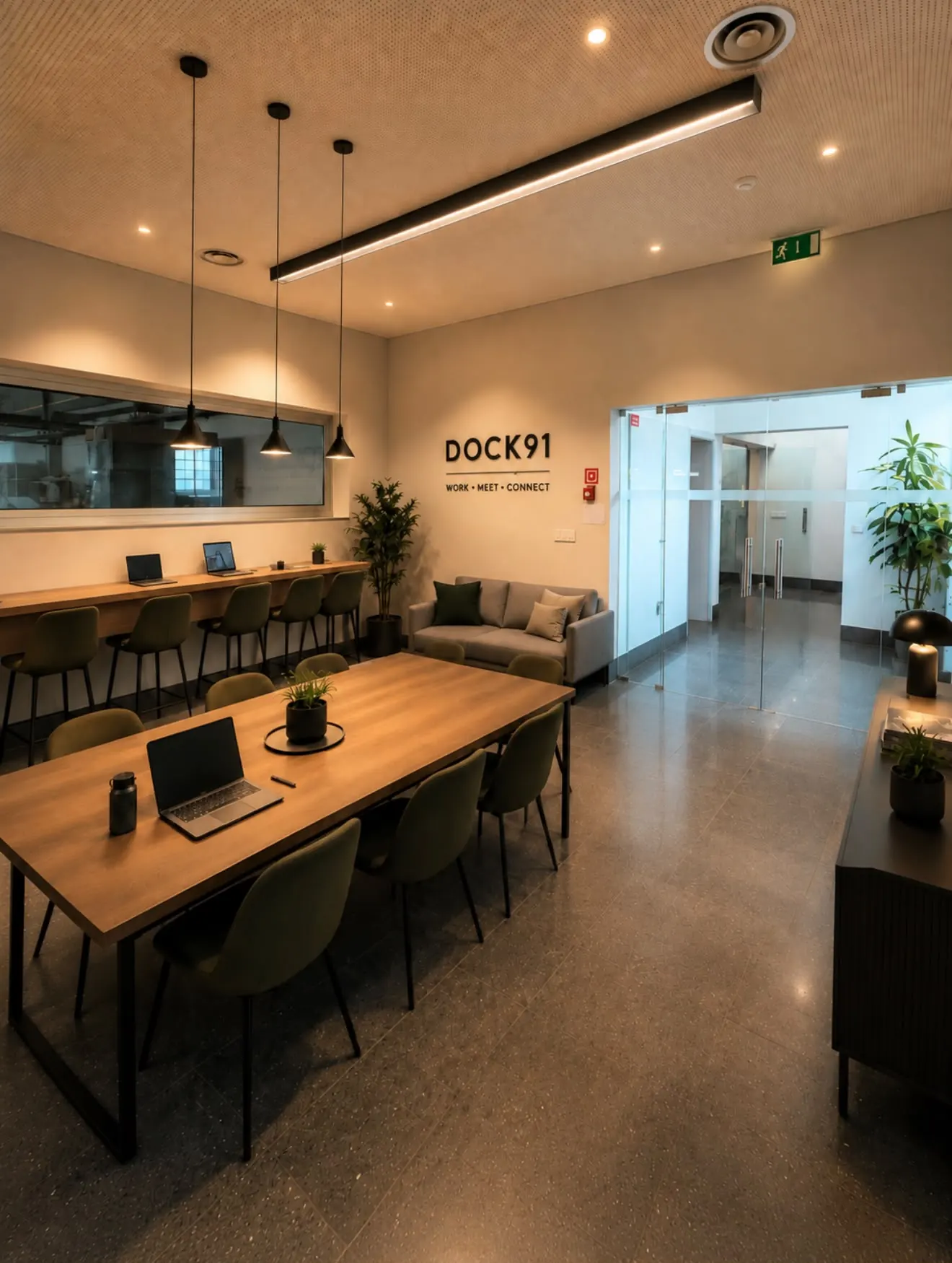 Zona comum do DOCK91 com mesa longa de madeira, cadeiras verdes, sofás e iluminação quente